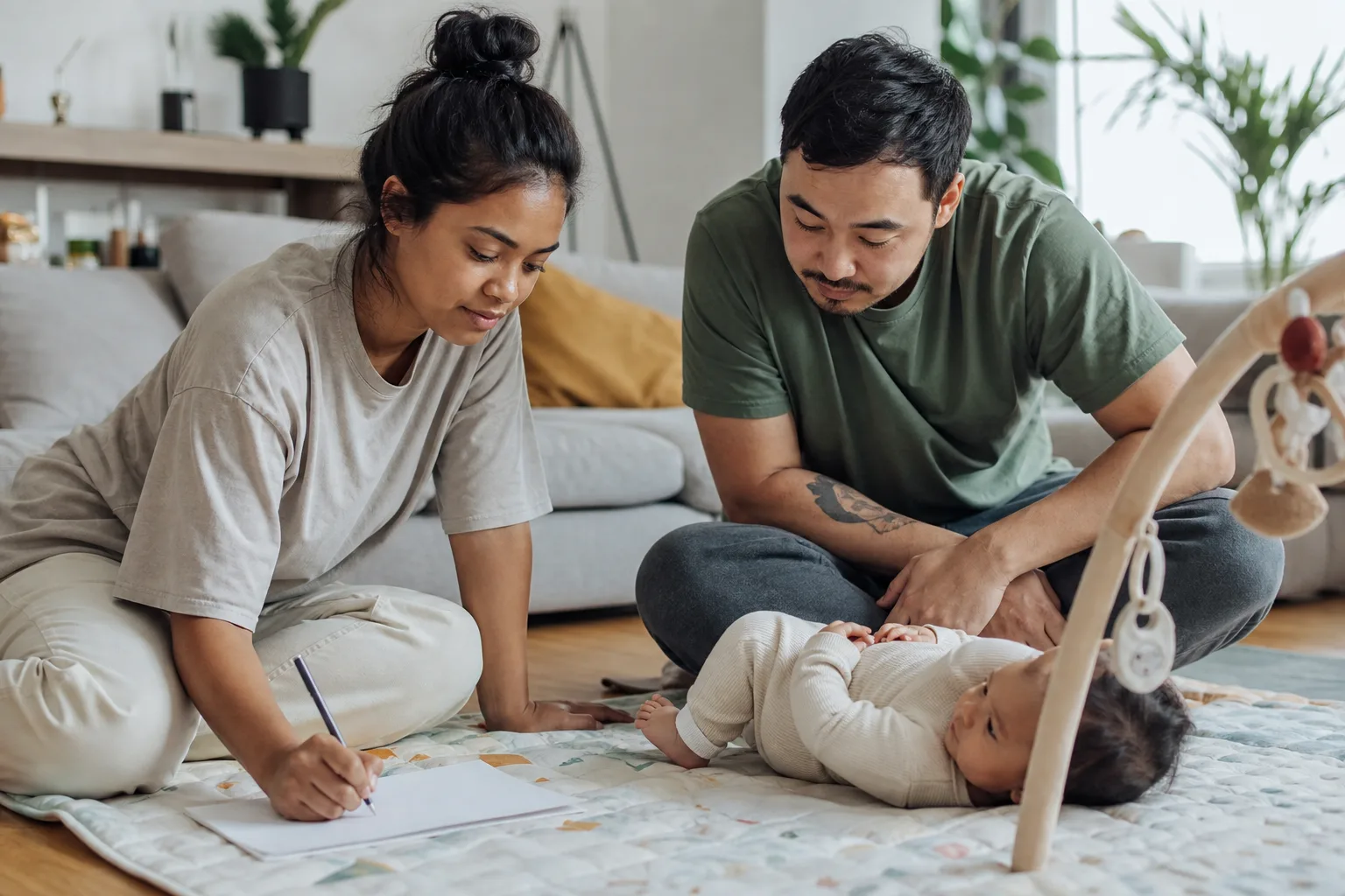 Two caregivers calmly observe their awake baby's face, hands, and posture while recording notes