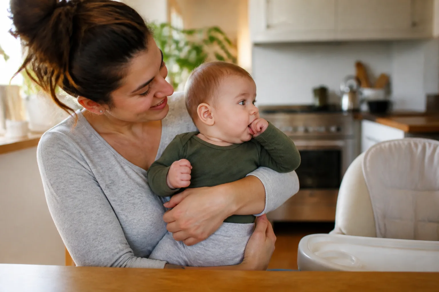Caregiver holds an alert baby who brings a hand to the mouth before crying